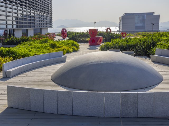 Installation artwork on a roof garden consisting of a grey hemisphere-shaped mound and several red three-dimensional forms, each big enough for a person to climb on. The red forms are tetrahedrons consisting of hexagonal sides with holes in the centre. The tetrahedrons are stacked on top of each other.